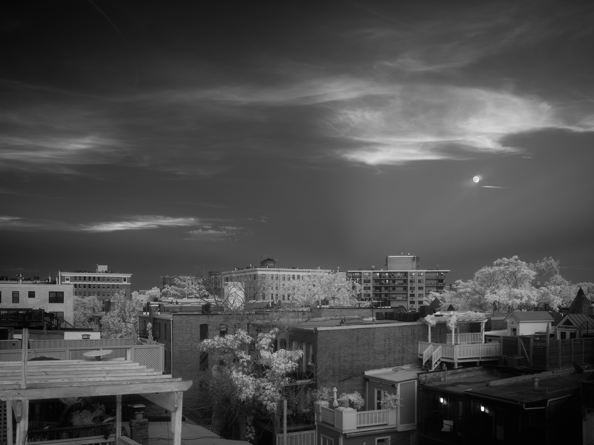 Clouds and a moon against a dark sky, over urban rooftops.