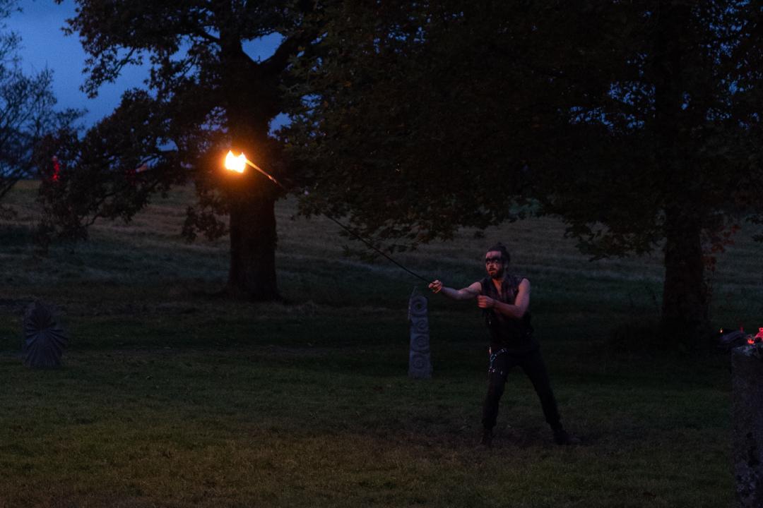 a photo of a fire throwing performer using a flame on a chain. he is launching the flame away from him, the chain taught. the fire casts some light into the otherwise quite dark scene