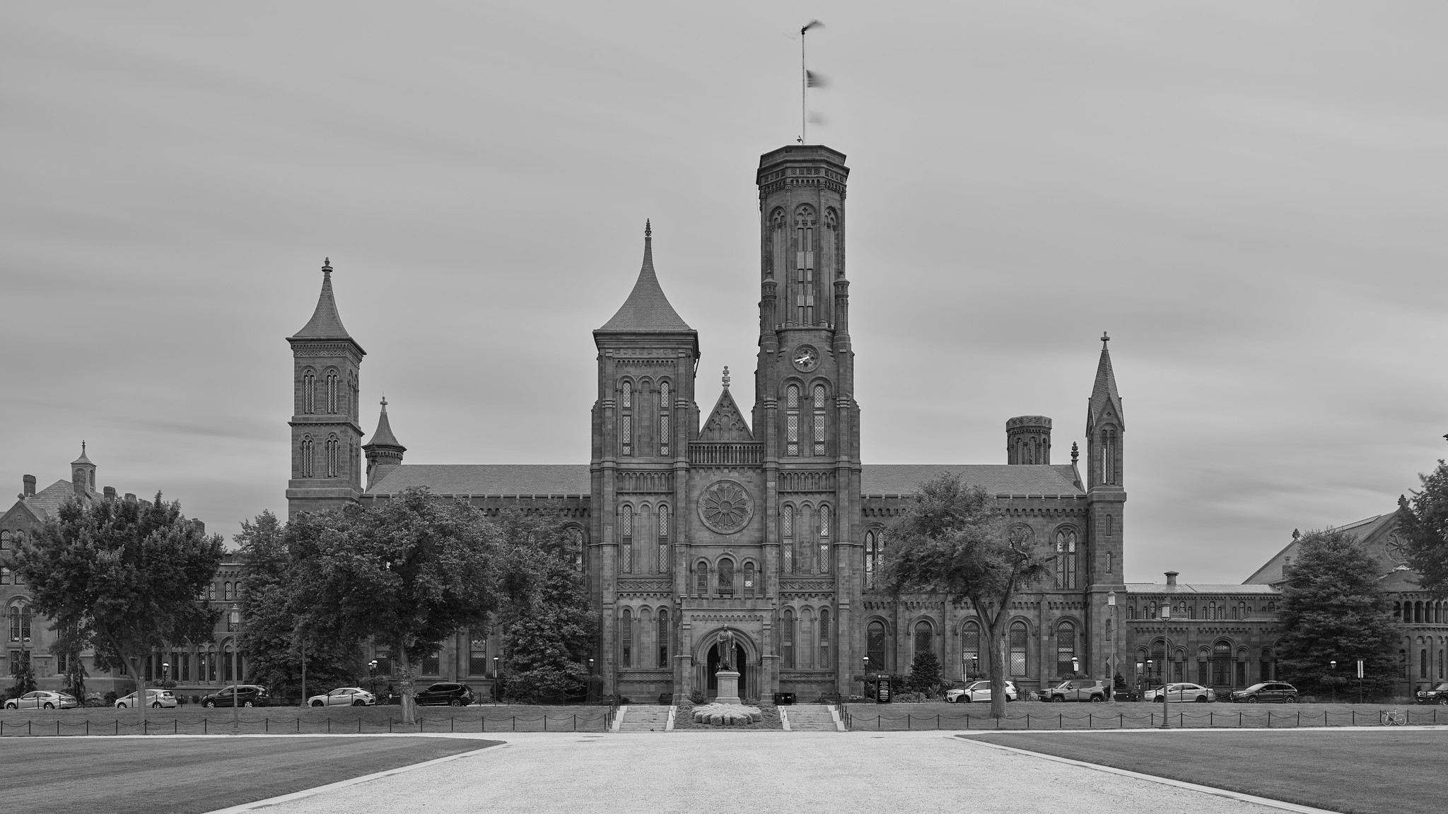 A medium-sized castle-like building, with turrets, flags, and a clock, across a plaza.