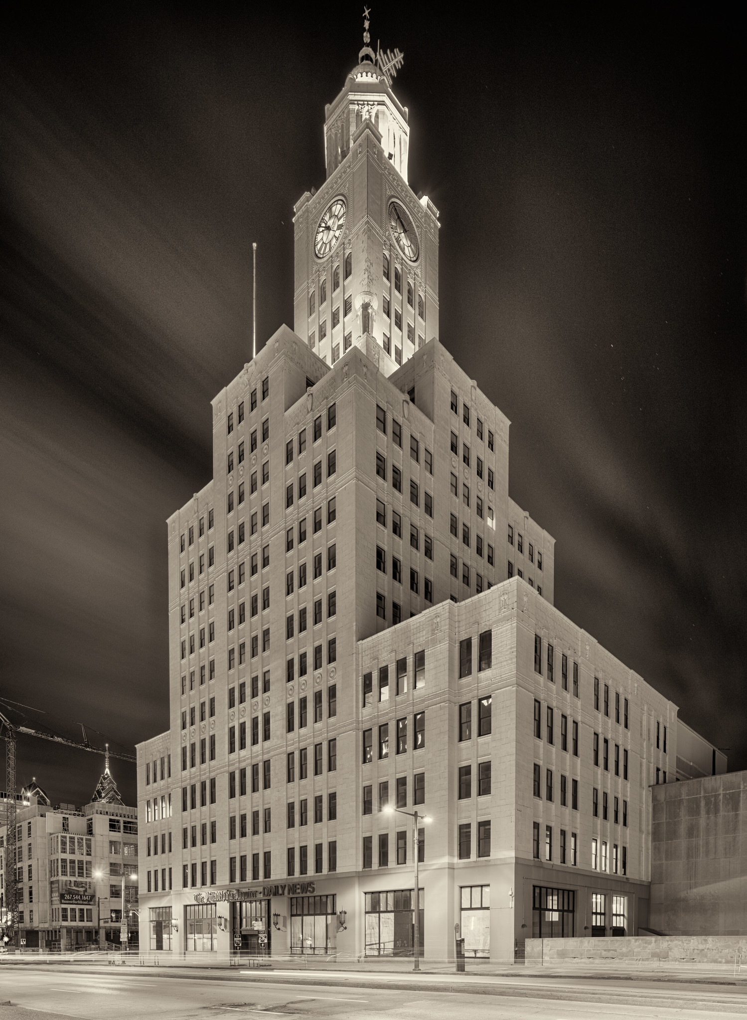 An early 20th century office building, with setbacks and a clock tower, at night.